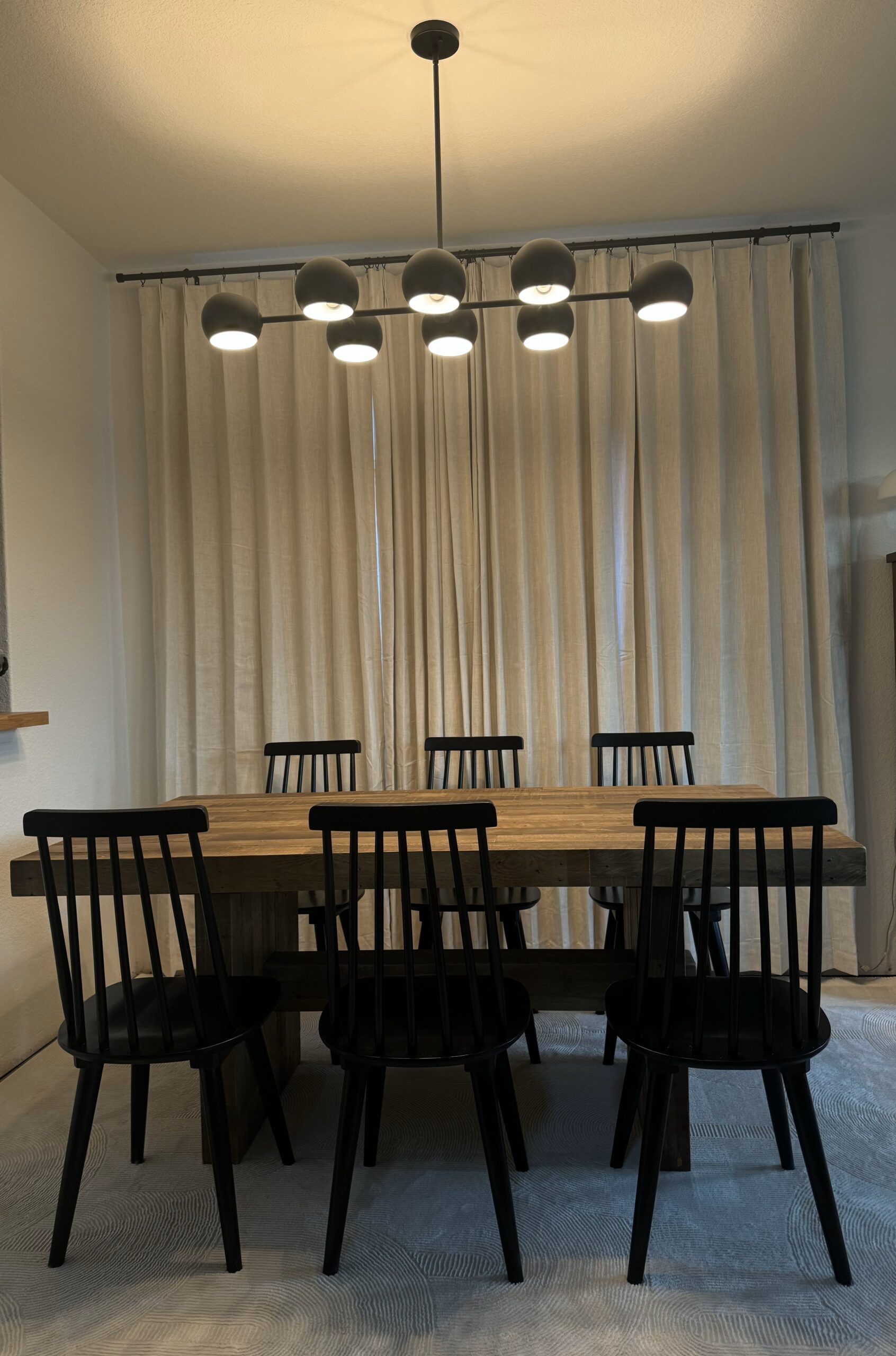 Dining room complete! Picturing our brand new dining light that is black with 8 dome lights... a reclaimed pine dining table, with 6 black wood chairs on a beautiful white area rug.